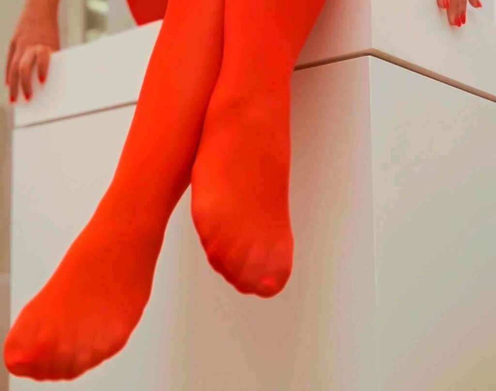 imagen de los pies de una mujer con las piernas cruzadas con unas medias rojas de nylon