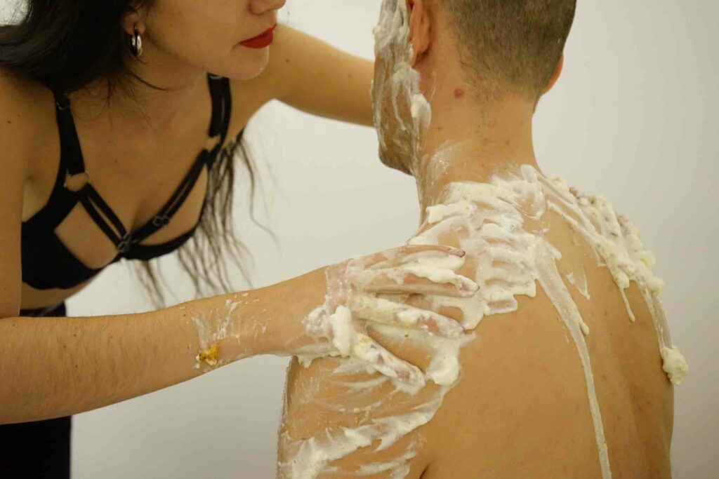 imagen de un hombre de espaldas y una mujer que le esparce nata sobre los hombros en una sesión de WAM