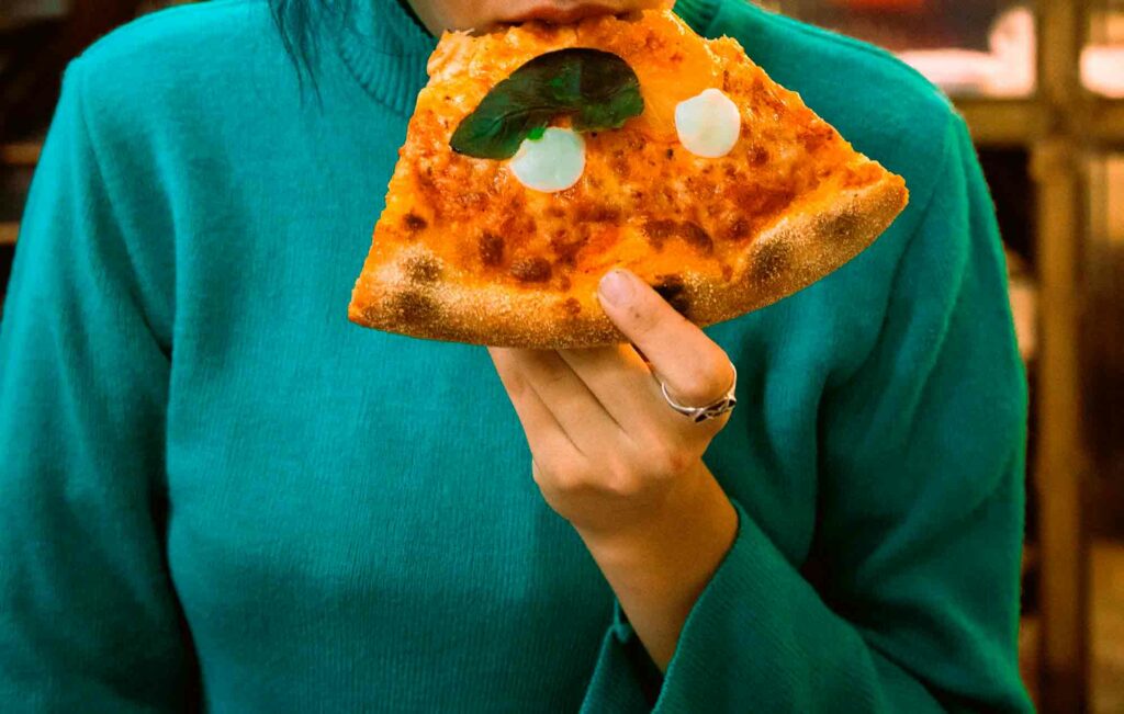 imagen de las manos de una mujer sujetando una porción de pizza para realizar la sesion de Feederism